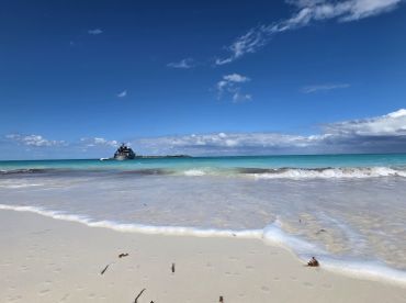 A stunning view of a boat anchored near a pristine beach, with turquoise waters and a clear blue sky, perfect for showcasing tropical destinations.
