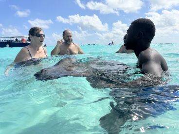 Guests interact with a stingray in the crystal-clear waters, creating a memorable wildlife experience in the Bahamas.