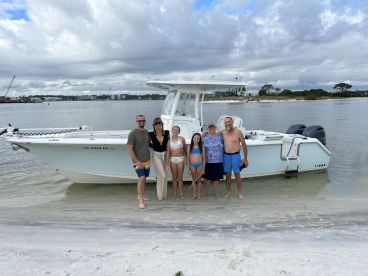 A joyful family poses together on the beach next to their boat, capturing a perfect day of fun and relaxation by the water.