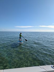 A child paddleboards across crystal-clear waters, showcasing a fun and adventurous day on the water — perfect for family outings and water sports enthusiasts.