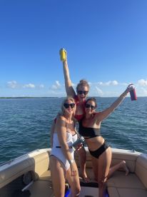 A lively group of friends celebrates on a boat, raising their drinks against a beautiful backdrop of the sea — perfect for summer parties and fun outings.