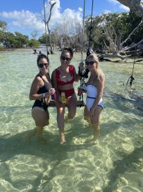 A fun group of friends enjoys a sunny day in the shallow waters, celebrating with drinks and laughter — perfect for a beach party atmosphere.