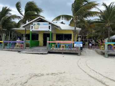A vibrant beachside bar with colorful seating and palm trees, creating a lively atmosphere for visitors enjoying the coastal setting.