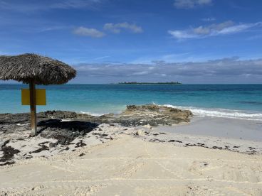 A serene beach scene featuring a thatched umbrella and stunning turquoise waters, perfect for relaxation and enjoying the natural beauty of the coastline.