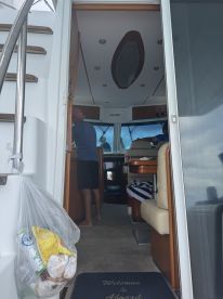 Inside view of a boat's cabin featuring a helm and seating area, with a guest preparing food. The welcoming atmosphere is perfect for relaxing during a day on the water.