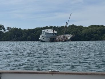 An abandoned boat wreck partially submerged near mangroves, showcasing the remnants of maritime history in a tranquil waterway.