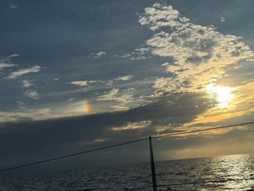 A stunning sunset over the ocean, with vibrant clouds and a hint of rainbow, creating a picturesque scene perfect for evening boat trips.