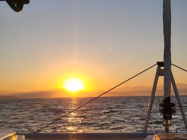 A stunning sunset view from the deck of a boat, showcasing the tranquil ocean and distant mountains — perfect for romantic evening cruises.