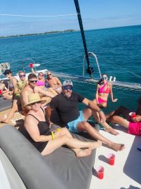 A lively group enjoys a day of sailing on a catamaran, relaxing with drinks and soaking up the sun — the perfect setting for a fun day on the water.