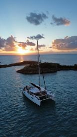 A stunning aerial view of a catamaran sailing at sunset, surrounded by tranquil waters and rocky outcrops, perfect for showcasing the beauty of sailing adventures.