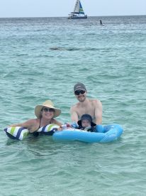 A joyful family enjoys a day at the beach, floating in the clear waters with a sailboat in the background — perfect for family fun and relaxation.