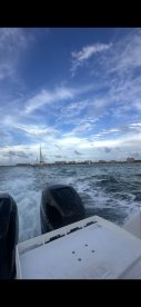 A scenic view from the back of a boat, showcasing the wake and a distant sailboat against a beautiful sky — perfect for capturing the essence of a day on the water.