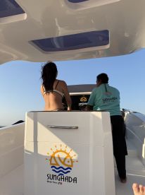A view of the helm area inside a boat, featuring two individuals preparing for a tour. The boat's branding is visible, indicating a professional boat tour service.