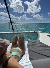 A woman relaxes on the deck of a catamaran, soaking up the sun with stunning ocean views — an ideal scene for a day of leisure on the water.