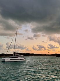 A serene view of a catamaran anchored in tranquil waters, set against a dramatic sky at sunset — perfect for showcasing luxury sailing experiences.