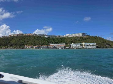 A picturesque view of a lush coastline and resort buildings from a boat, showcasing the vibrant turquoise waters and scenic landscape — perfect for island hopping adventures.