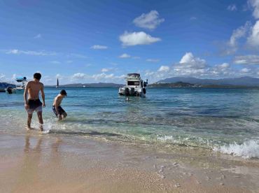 Two boys enjoy a sunny day at the beach, splashing in the shallow water near a boat — a perfect scene for family fun and summer adventures.