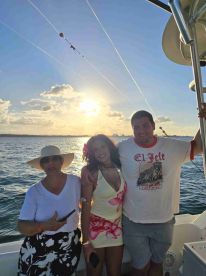 A joyful group poses for a photo on a boat during sunset, capturing a memorable moment of celebration on the water.