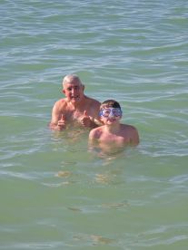 A joyful moment captured as a grandfather and grandson enjoy swimming together in clear waters, showcasing the fun of family bonding during a day at the beach.