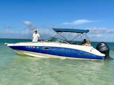 A man stands proudly on a NauticStar boat while another person relaxes onboard, showcasing a perfect day at the beach.