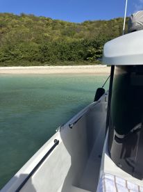 A serene view of a boat alongside a tranquil beach, showcasing the clear waters and lush greenery in the background — perfect for a day of relaxation on the water.