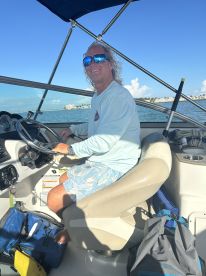 A smiling captain navigates from the helm of a boat, showcasing the comfortable interior and steering controls, perfect for a day on the water.