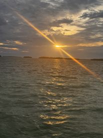 A stunning sunset casts golden rays over the water, with distant islands silhouetted against the colorful sky — a perfect backdrop for evening boat trips.