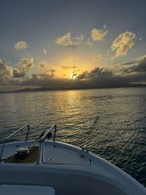 A serene sunset view from the bow of a boat, showcasing the tranquil waters and distant mountains — perfect for peaceful evening cruises.
