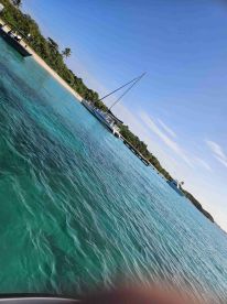 A picturesque view of a sailboat anchored near a sandy beach, surrounded by crystal-clear waters — perfect for a relaxing day on the water.