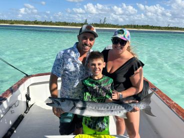 A family proudly displays their catch of the day, a barracuda, while enjoying a fishing trip in crystal-clear waters — a perfect family adventure on the boat.