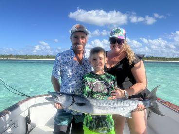 A family proudly displays their catch of the day, a barracuda, while enjoying a fishing trip in crystal-clear waters — a memorable moment on the water.