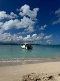 A scenic view of a boat docked near a sandy beach, surrounded by clear turquoise waters and a beautiful sky — perfect for a relaxing day on the water.