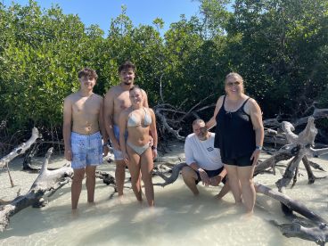 A joyful family poses together in shallow water surrounded by mangroves, capturing a fun beach day filled with laughter and adventure.