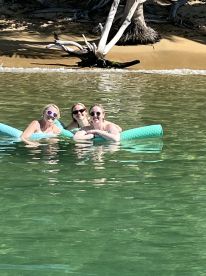 Three friends enjoy a sunny day floating on mats in clear waters, perfect for a fun day out on the water.