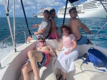 A joyful family enjoys a day out on the water, relaxing and having fun aboard their boat, with cruise ships visible in the background.