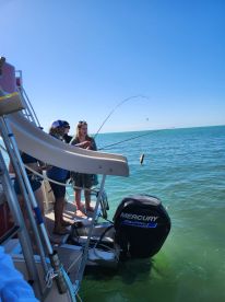 A group of friends enjoys a fishing adventure on the water, showcasing the excitement of reeling in a catch. Perfect for those looking to experience fun and camaraderie on a boat.