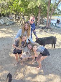 A family interacts with friendly pigs on the beach, creating a memorable wildlife experience in a tropical setting.