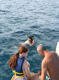 A group enjoys snorkeling in clear waters, with one person actively exploring underwater while others prepare to join — a perfect adventure for water enthusiasts.