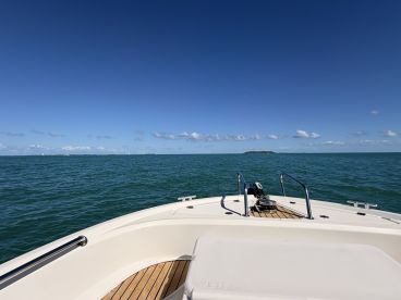 A clear view from the front of a boat cruising through calm waters, showcasing a beautiful blue sky and distant islands — perfect for a day out on the water.