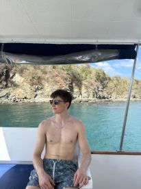 A young man relaxes on a boat, enjoying the scenic views of the coastline — perfect for a day of leisure on the water.