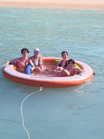 A joyful group of friends enjoys a sunny day floating on a mat in clear waters, perfect for summer fun and relaxation.