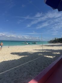 A scenic beach view featuring boats anchored offshore and guests enjoying the sun, perfect for a relaxing vacation atmosphere.