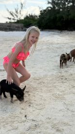 A young girl interacts with a pig on the beach, showcasing a delightful moment of human-animal interaction — a popular experience in the Bahamas.