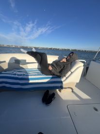 A person relaxes on a comfortable seating area inside a boat, enjoying the serene water views — perfect for unwinding during a day on the water.