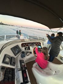 A young girl takes the helm of a boat while family members enjoy the view from the cabin, showcasing the excitement of boating adventures.