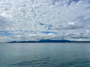 A serene view of the coastline under a dramatic sky, showcasing the tranquil waters and distant mountains — perfect for capturing the beauty of nature on a boating trip.
