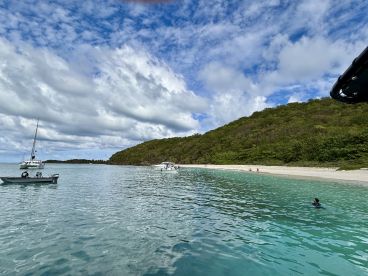 A picturesque view of boats anchored near a serene beach, with a swimmer enjoying the clear waters — perfect for island hopping adventures.