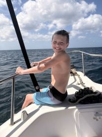 A young boy enjoys a sunny day on the boat, smiling as he takes in the ocean views — a perfect moment of joy on the water.