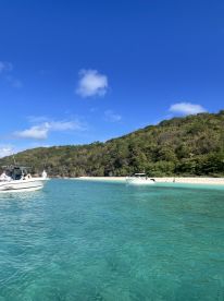 A picturesque view of boats anchored in crystal-clear turquoise waters near a sandy beach, perfect for island hopping adventures.