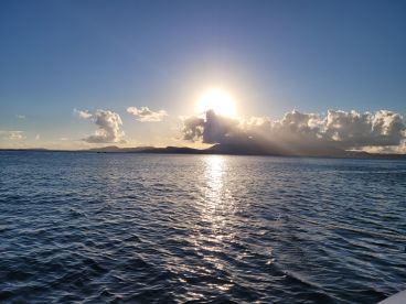 A stunning sunset over the coastline, casting golden reflections on the water — a perfect moment for serene boat trips or evening cruises.